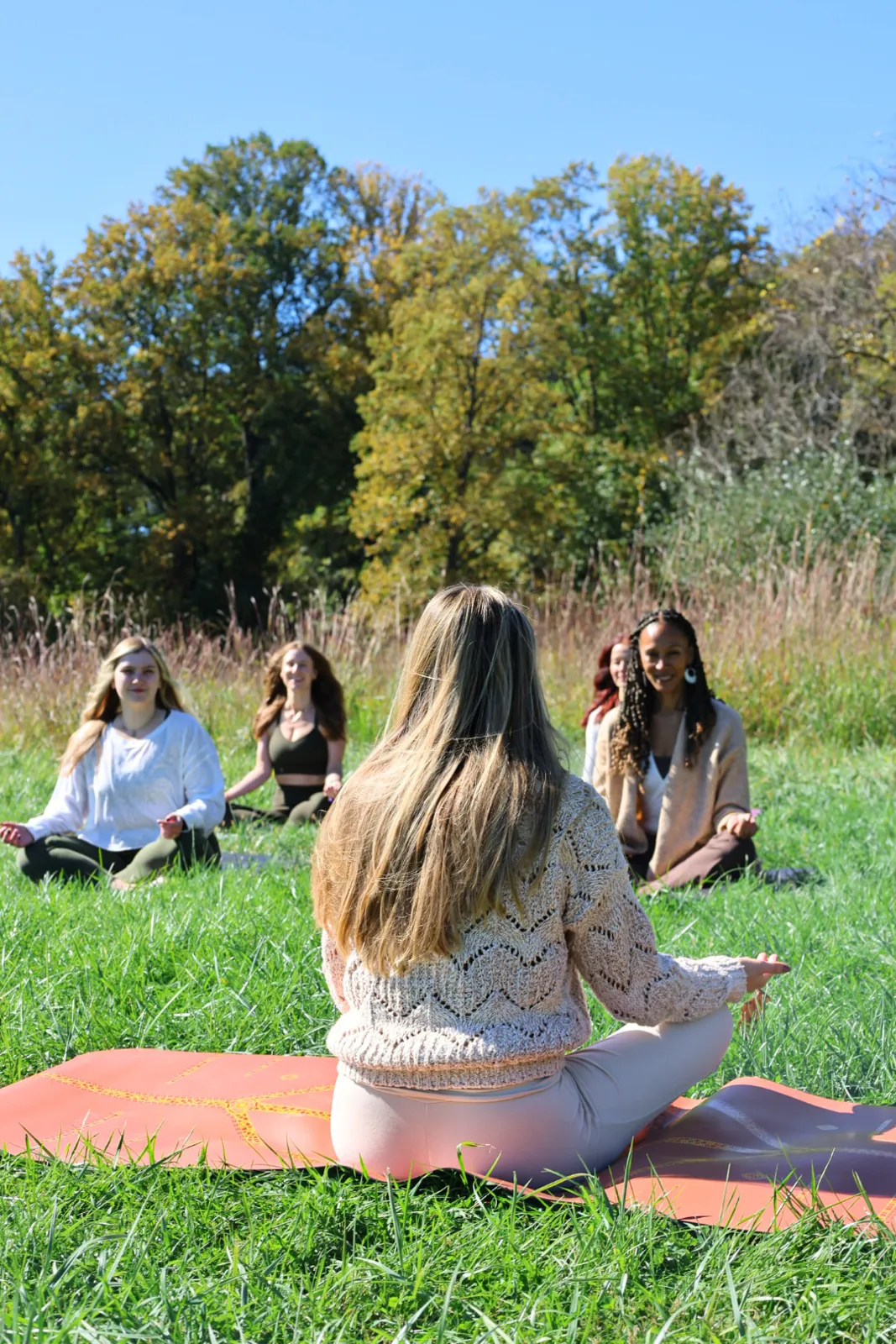 Students seated on mats listening to a teacher in a meadow