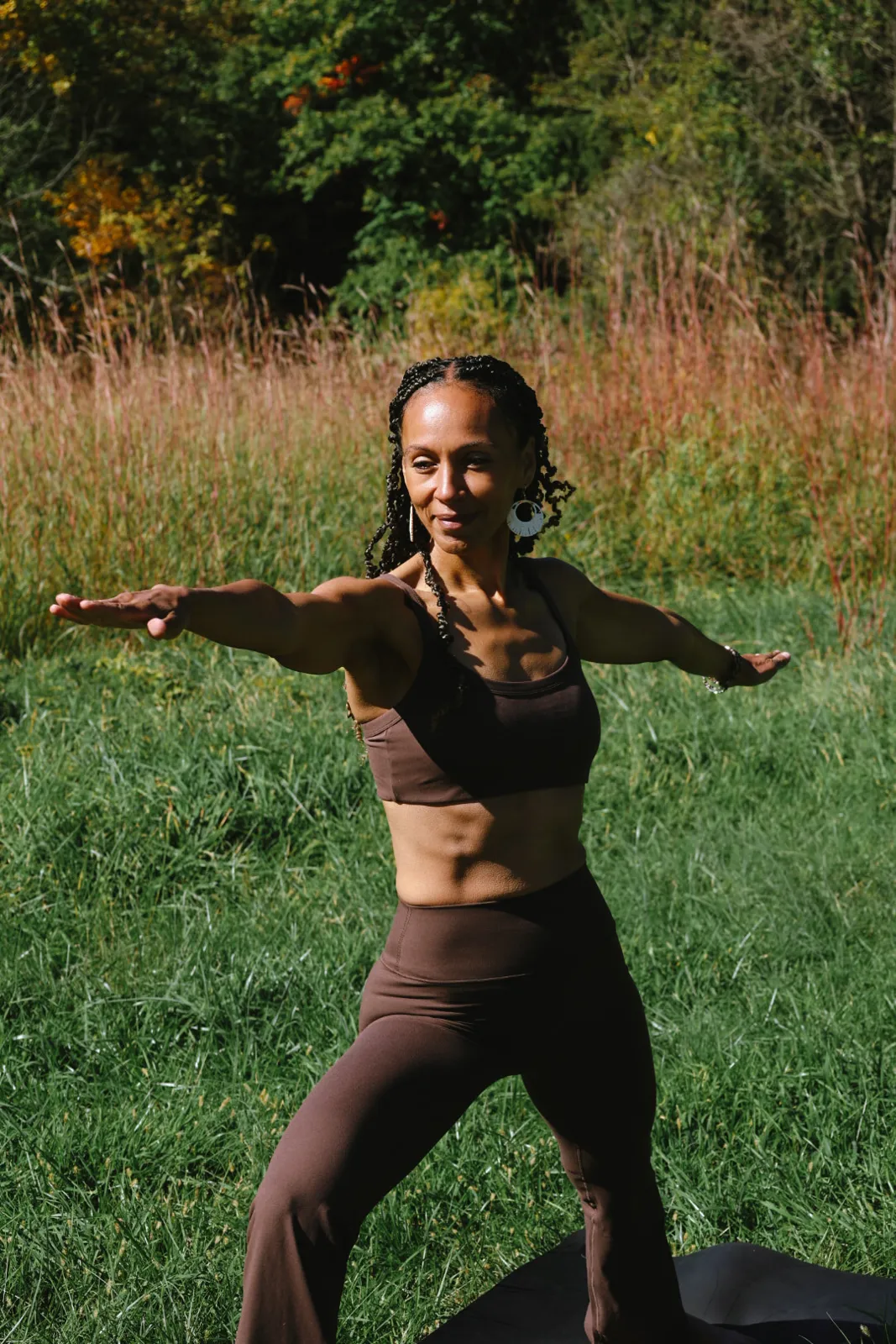 Woman holding warrior two pose in a green field