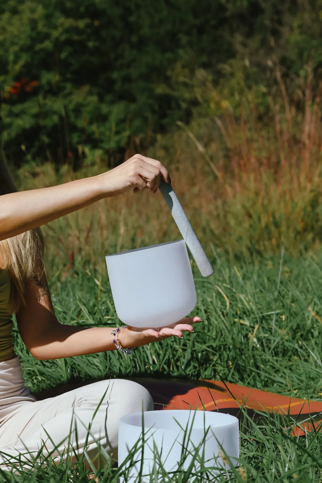 Teacher playing a crystal singing bowl on a mat in the grass