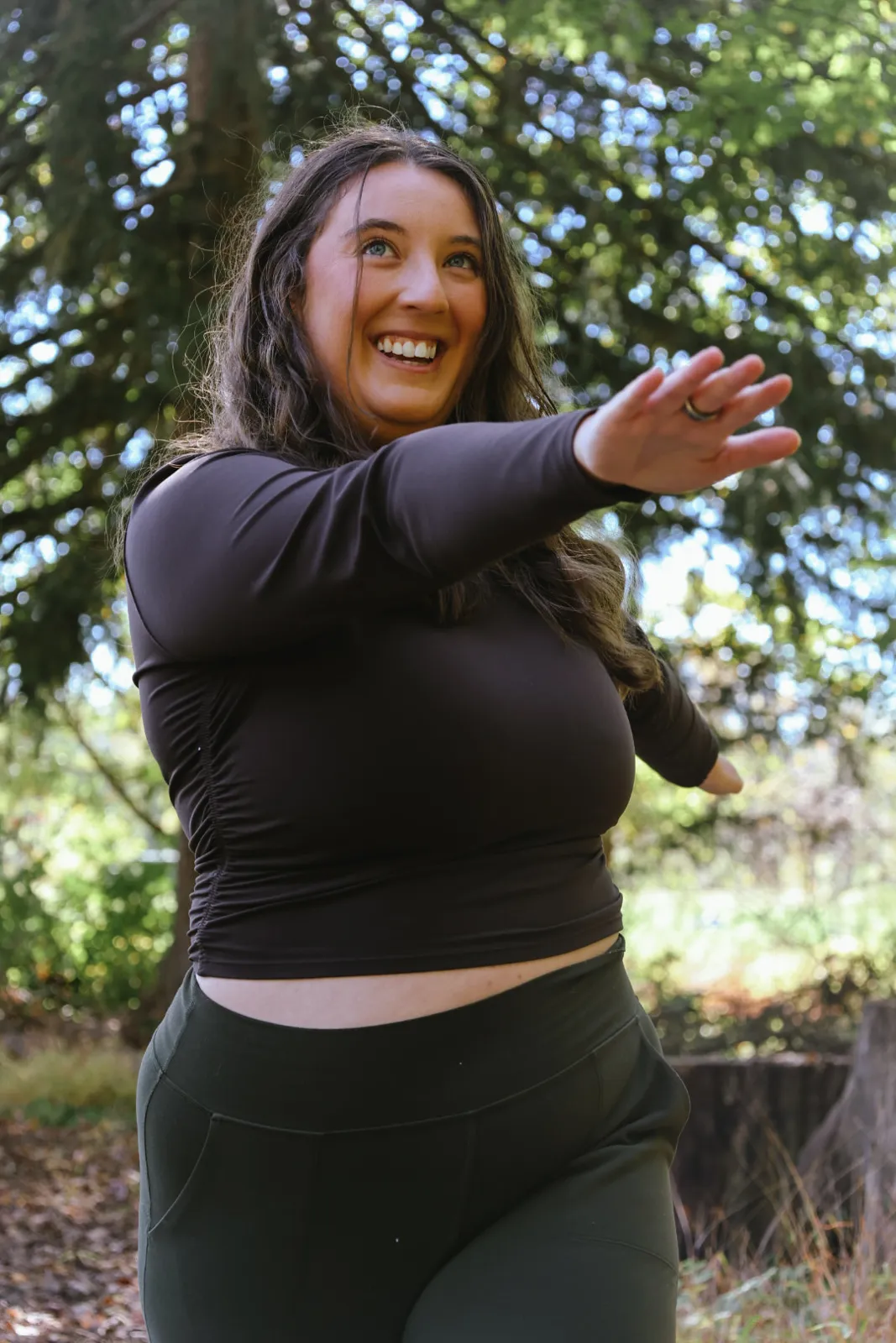 Smiling woman opening her arms in a wooded clearing